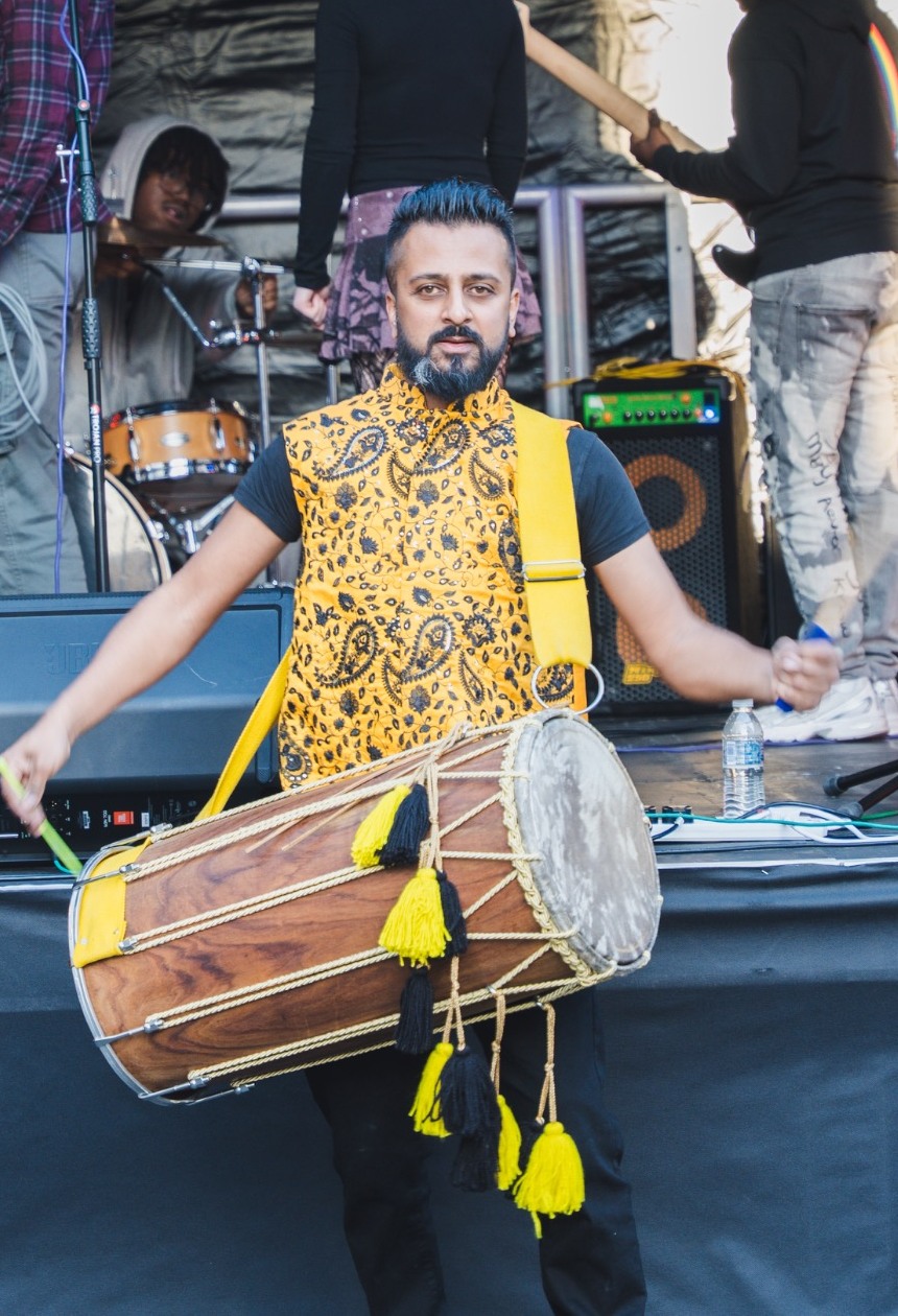 Dhol drummer performing with yellow tasselled drum